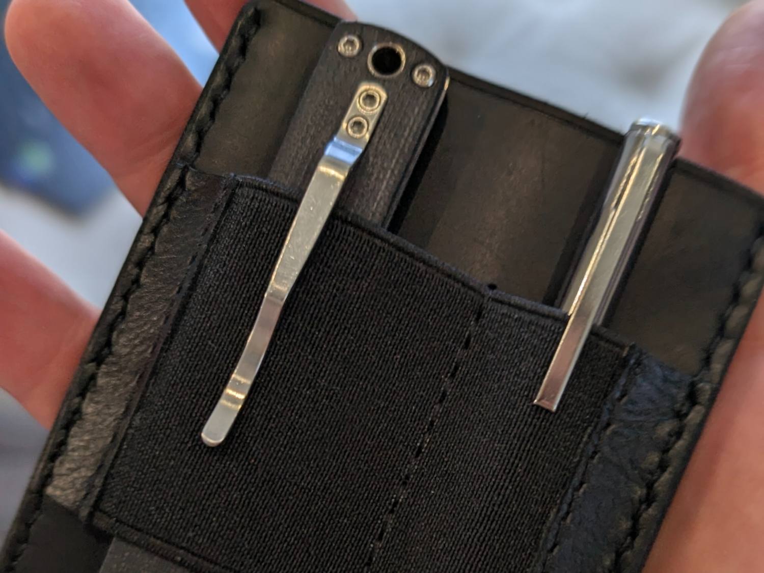 A hand holding the black leather MRF holder loaded with a folding knife and a pen under its elastic band